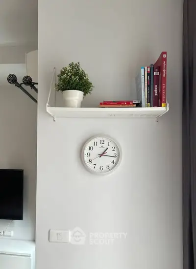 Modern interior with wall clock, shelf, and books in stylish living room.