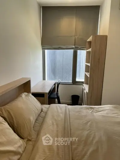 Cozy bedroom with natural light, featuring a bed, desk, and shelving unit.