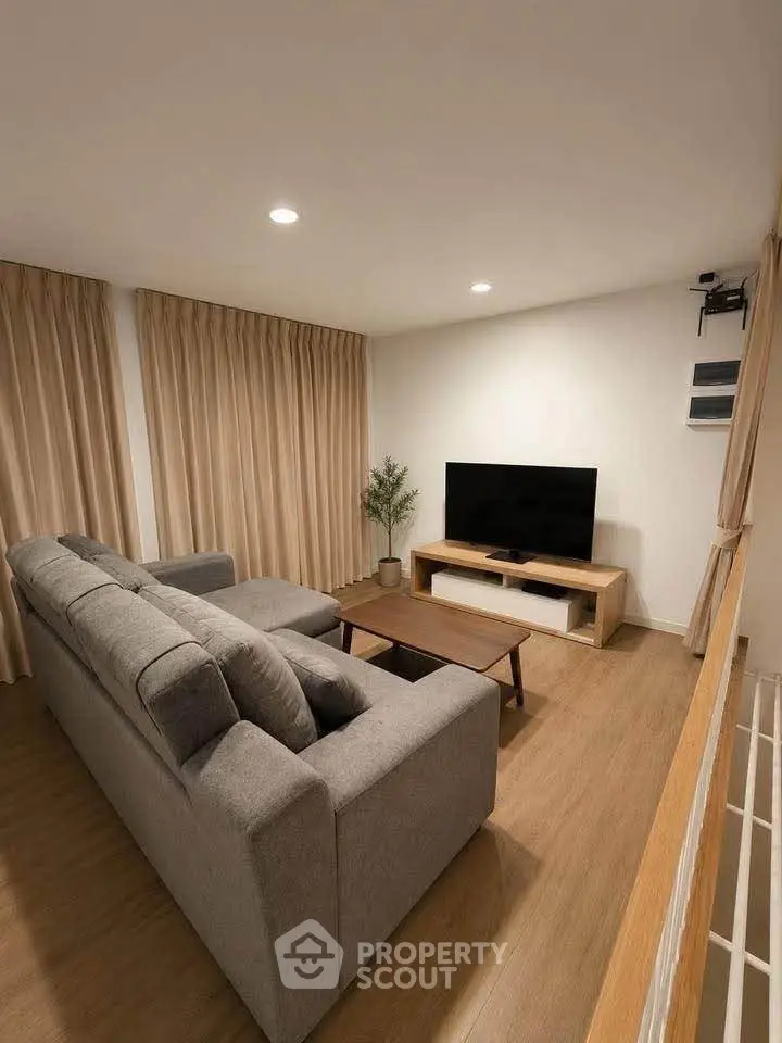 Modern living room with cozy gray sofa, wooden flooring, and large TV setup, perfect for relaxation.