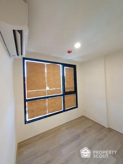 Bright empty room with wooden flooring and large window, perfect for customization.