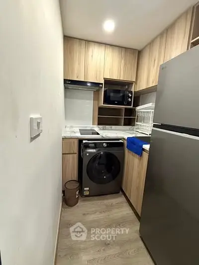 Modern compact kitchen with wooden cabinets, washing machine, and sleek appliances.