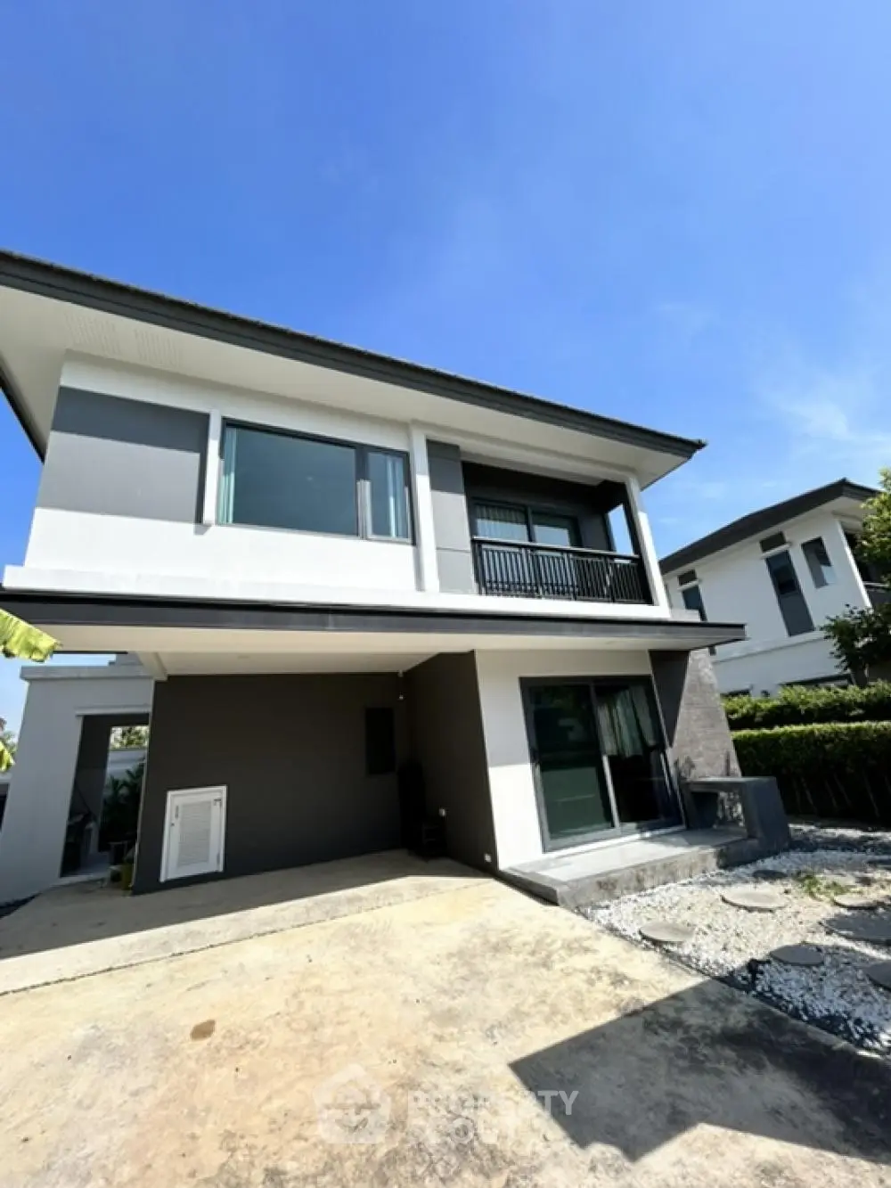 Modern two-story house with sleek design and spacious driveway under clear blue sky.