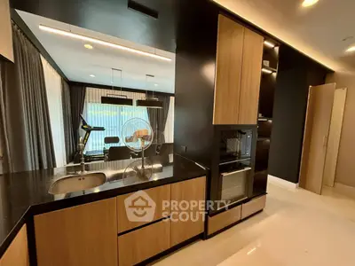 Modern kitchen with sleek black countertops and wooden cabinetry, open layout to living area with exercise equipment.