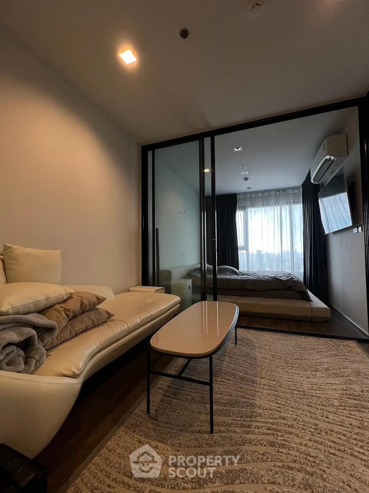 Modern living room with cozy sofa and glass partition leading to a stylish bedroom.