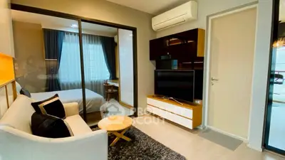 Modern living room with cozy sofa, TV, and view into stylish bedroom through glass partition.