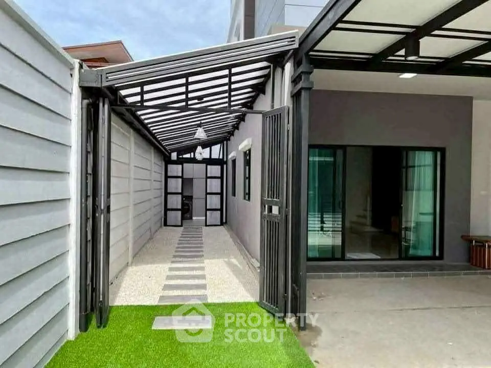 Modern home exterior with sleek design and covered walkway, featuring glass doors and artificial grass.