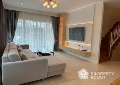 Modern living room with stylish sofa and wall-mounted TV, featuring elegant lighting and staircase.