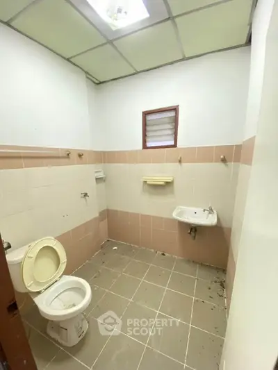 Spacious bathroom with tiled walls and floor, featuring a toilet and sink, ideal for renovation.