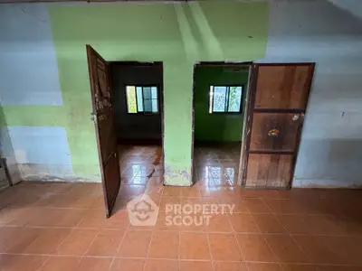 Spacious interior with tiled flooring and two wooden doors leading to separate rooms, ideal for renovation.