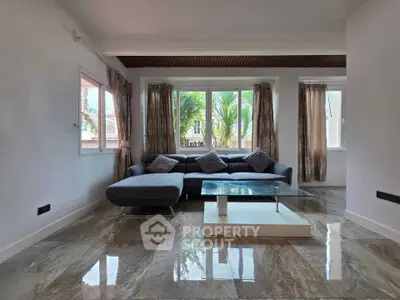 Spacious living room with modern sofa and glass coffee table, featuring large windows and elegant curtains.