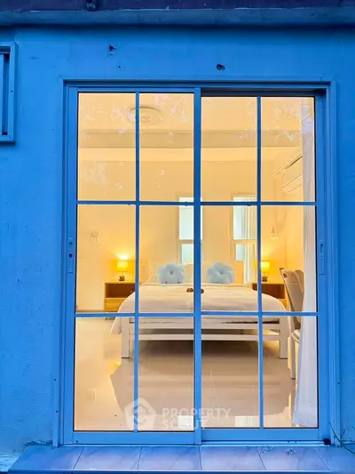 Cozy bedroom view through large glass doors with warm lighting and stylish decor.