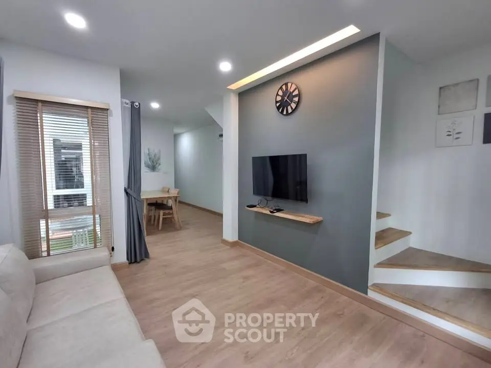 Modern living room with stylish decor and wooden flooring, featuring a wall-mounted TV and cozy seating area.