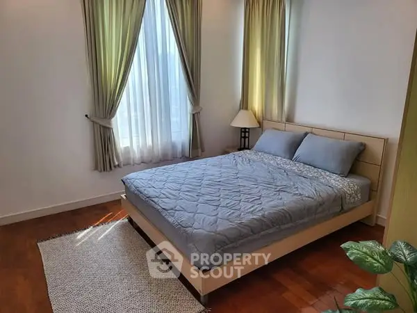 Cozy bedroom with natural light, wooden flooring, and elegant curtains.