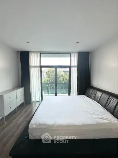 Spacious bedroom with large window and modern furnishings, offering a serene view.