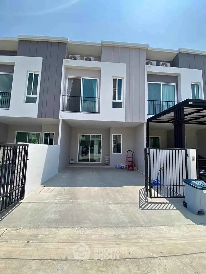 Modern townhouse exterior with sleek design and spacious driveway under clear blue sky.