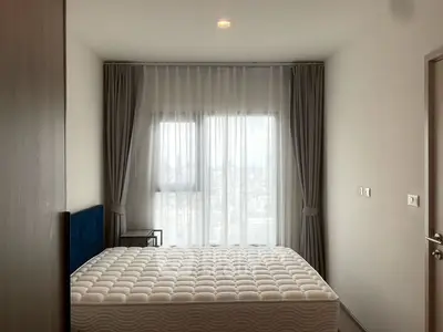 Modern bedroom with large window and city view, featuring a comfortable bed and elegant curtains.