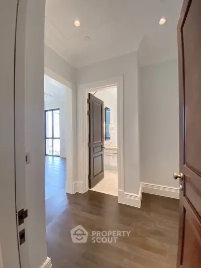 Elegant hallway with dark wood flooring and open doors leading to bright rooms.