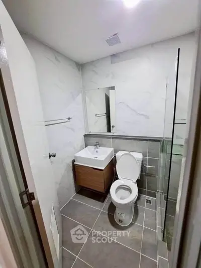 Modern bathroom with sleek design, featuring a white sink, toilet, and glass shower enclosure.