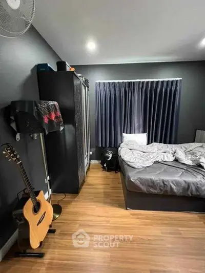 Cozy bedroom with wooden flooring, stylish dark curtains, and a guitar for a musical touch.