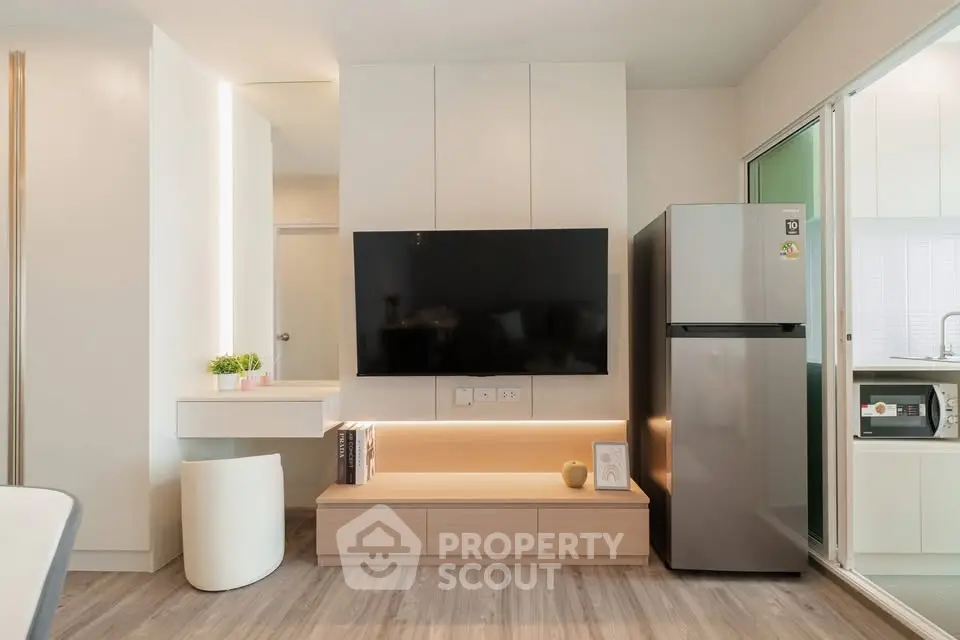 Modern living room with sleek TV setup and stainless steel fridge in stylish apartment.