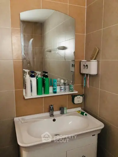 Modern bathroom with sleek sink and mirror, featuring tiled walls and organized toiletries.
