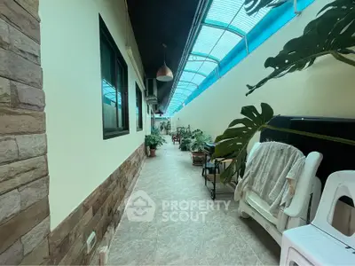 Charming covered outdoor corridor with lush plants and cozy seating area, perfect for relaxation.