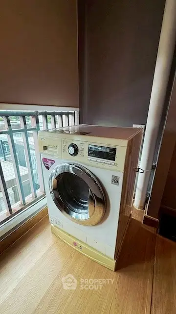 Modern washing machine in a bright laundry area with wooden flooring and large window.