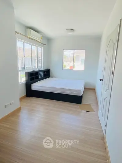 Bright bedroom with large windows and wooden flooring, featuring a modern bed frame and air conditioning.