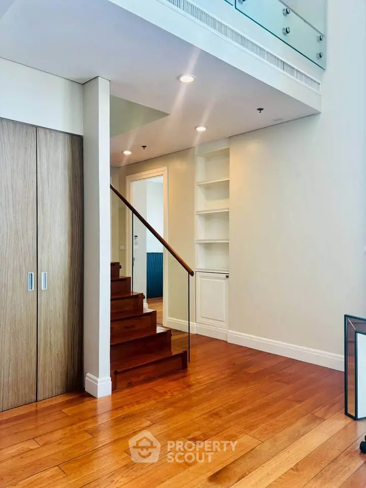 Modern duplex interior with wooden staircase and built-in shelving, featuring sleek design and ample natural light.