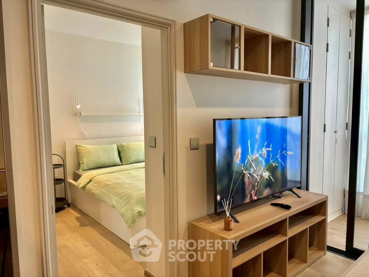 Modern apartment interior with cozy bedroom and stylish living area featuring a large TV and wooden shelving.