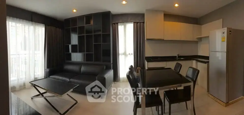 Modern living room with sleek black furniture and open kitchen layout in a stylish apartment.