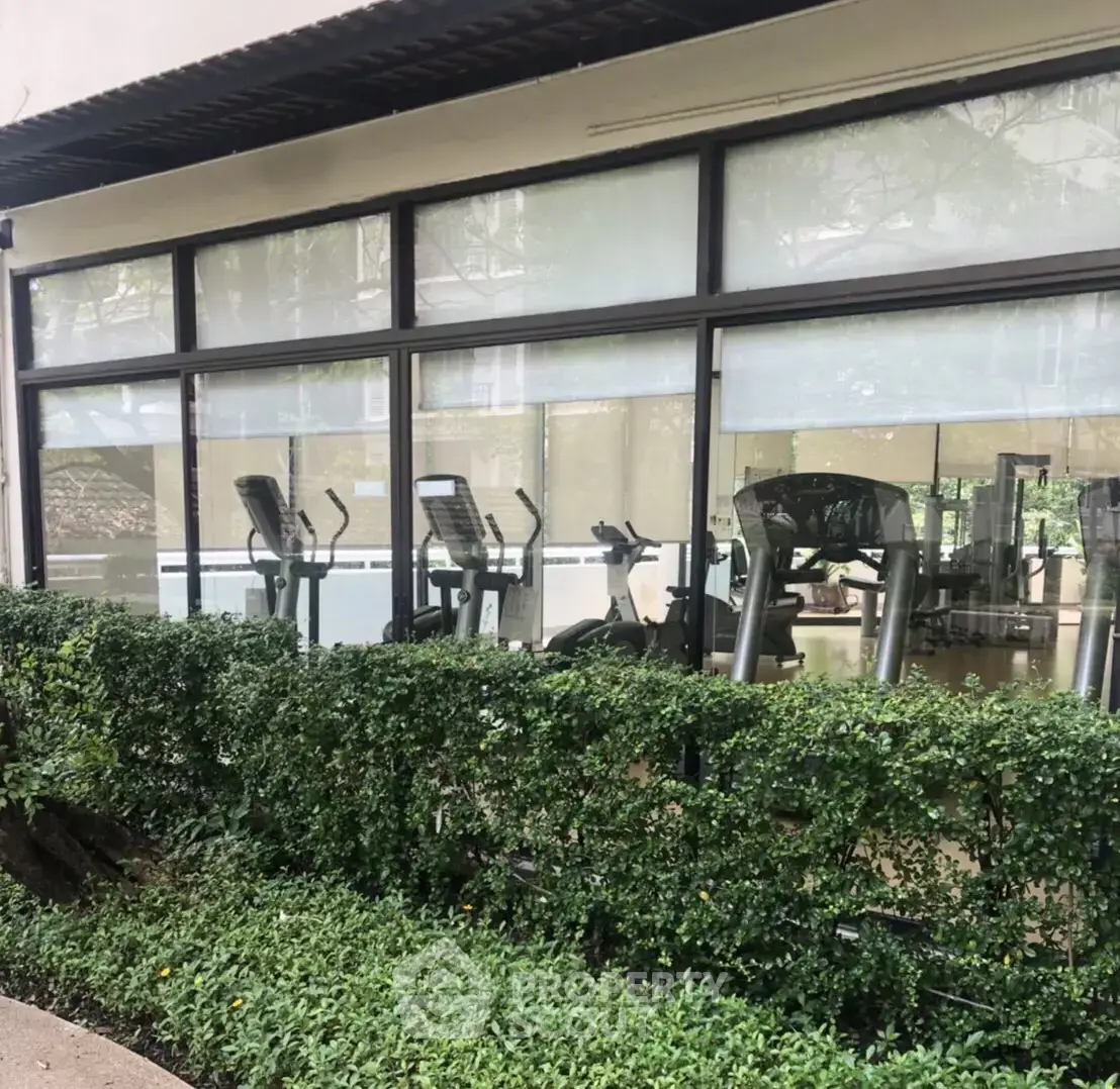 Modern gym with large windows and lush greenery in a residential building.