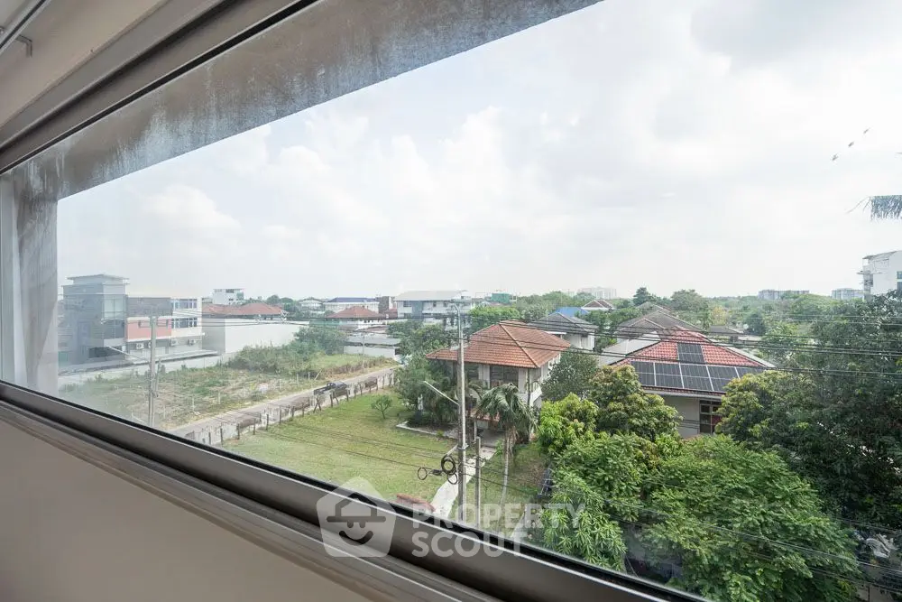 Stunning view from a modern window overlooking lush greenery and residential rooftops.