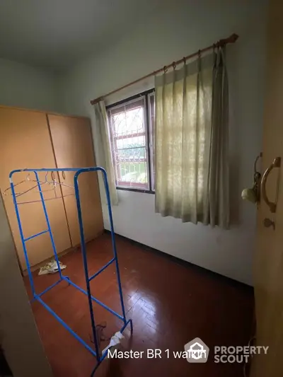 Cozy bedroom with potential for personalization, featuring hardwood floors, large window with classic curtains, and ample storage space.