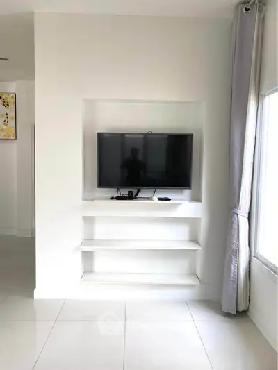 Modern living room with built-in TV and sleek white shelves, bright natural light from large window.