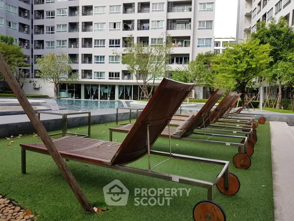 Luxurious apartment complex with poolside lounge chairs and lush greenery.