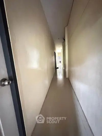 Narrow hallway with minimalist design and neutral tones, leading to a bright room.