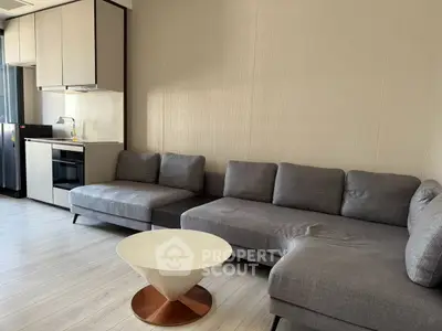 Modern living room with sleek gray sectional sofa and compact kitchen area featuring built-in oven.