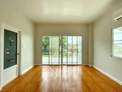 Spacious room with wooden flooring and large windows opening to a balcony.