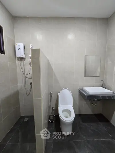 Modern bathroom with sleek tiles and contemporary fixtures, featuring a toilet and wall-mounted sink.
