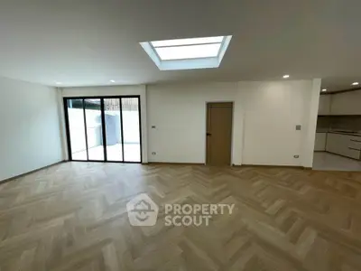 Spacious modern living room with skylight and herringbone flooring, adjacent to a sleek kitchen.