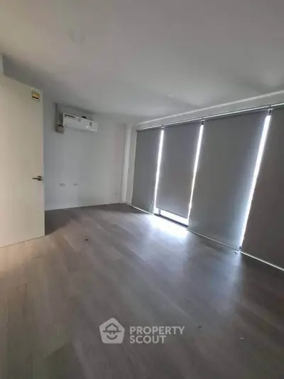 Spacious empty room with modern flooring and large windows with blinds, perfect for customization.