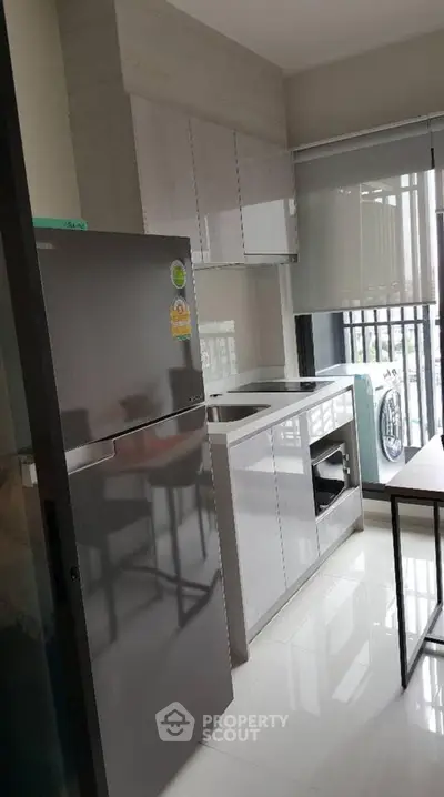 Modern kitchen with sleek cabinets, fridge, and balcony view in a stylish apartment.