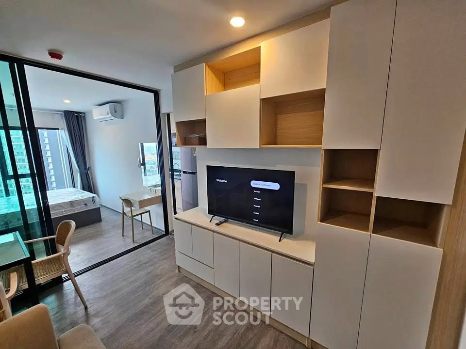 Modern living room with built-in storage and TV, open view to bedroom and balcony.