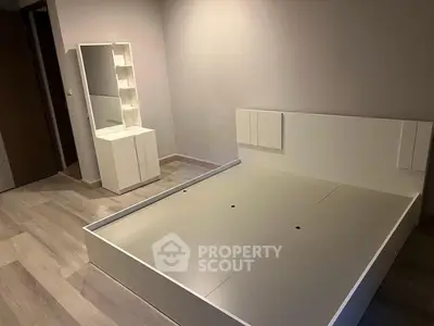 Modern minimalist bedroom with sleek white furniture and wooden flooring.