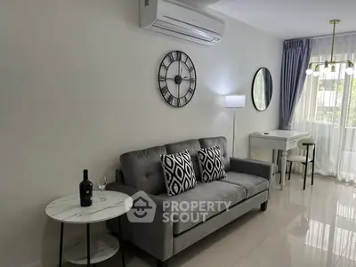 Modern living room with stylish decor, featuring a gray sofa, wall clock, and large window for natural light.