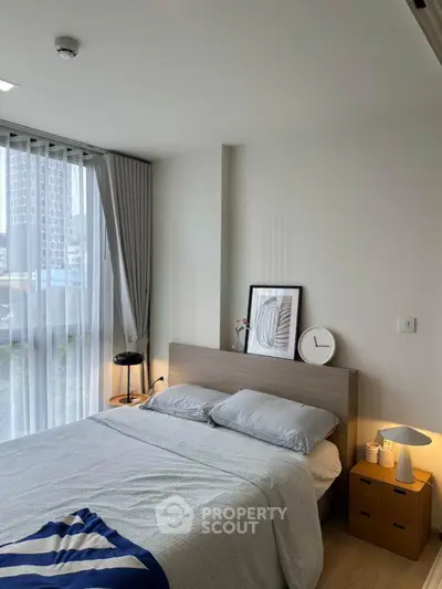 Modern bedroom with large window, stylish decor, and natural light in urban apartment.