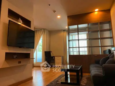 Modern living room with cozy seating and large TV, featuring stylish shelving and natural light.