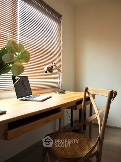Cozy study room with wooden desk, chair, and natural light from window blinds.