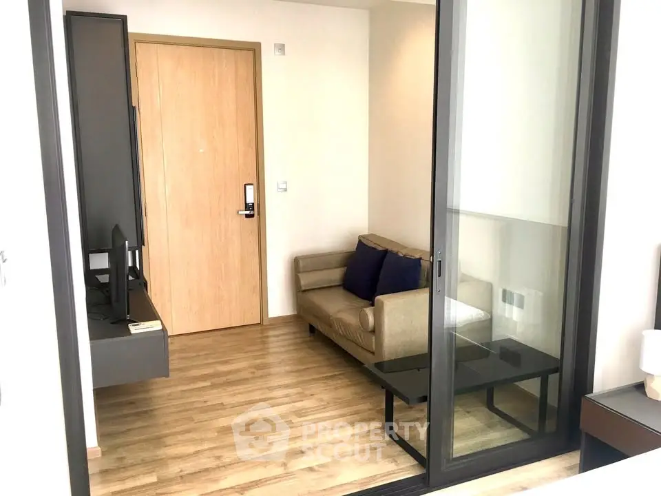 Modern living room with sleek design and wooden flooring, featuring a cozy sofa and glass sliding door.
